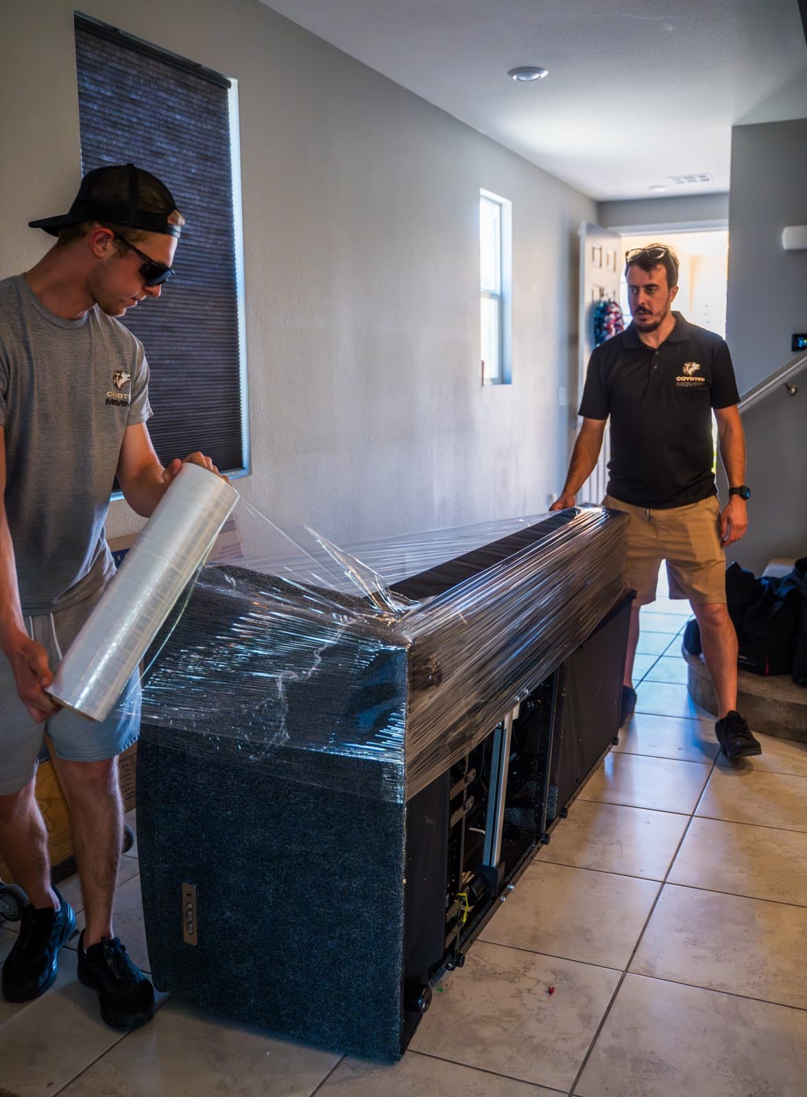 Coyotes Moving crew carrying a wrapped sofa down the truck ramp in a gated Henderson neighborhood with tile-roof homes