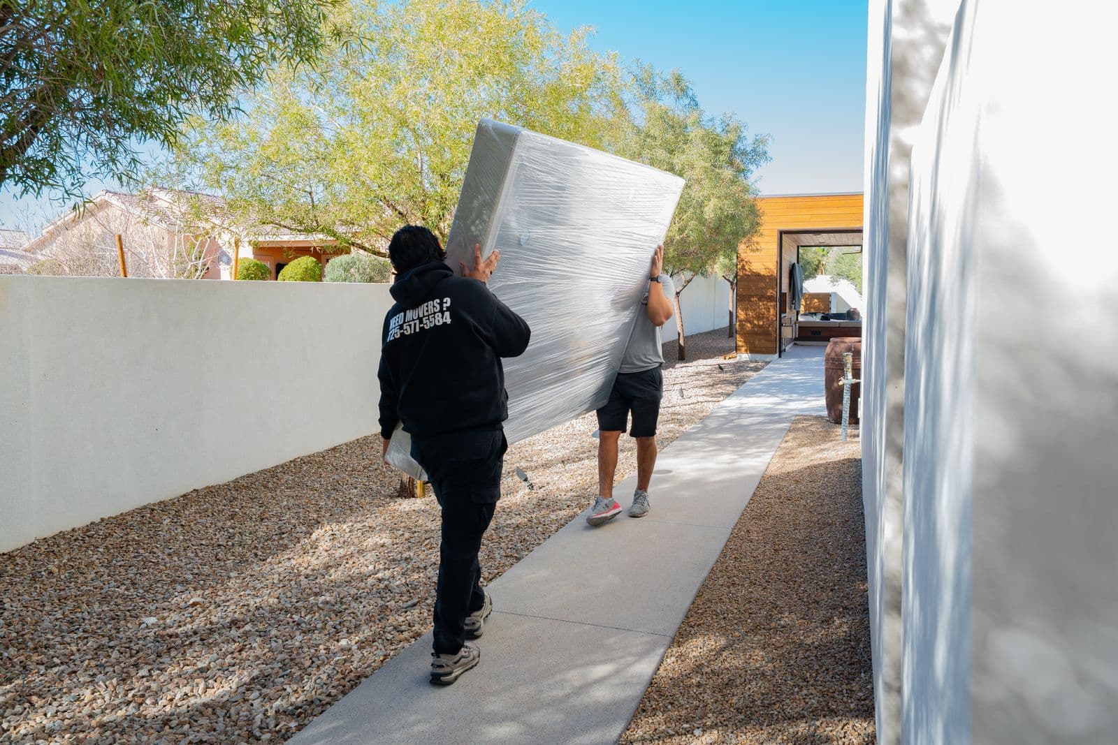 Coyotes Moving crew calmly carrying a wrapped mattress through a modern Las Vegas backyard during a move